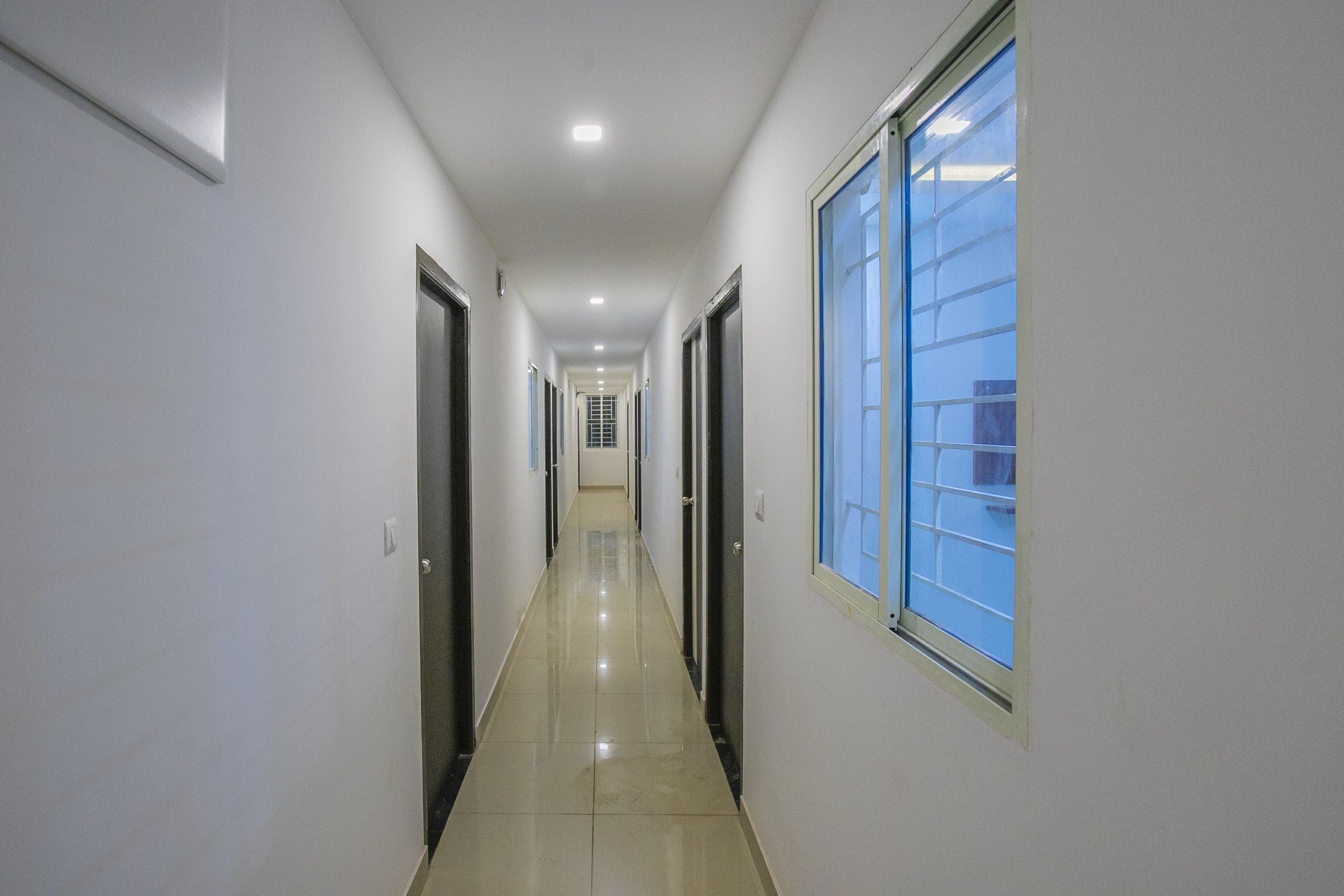 A long, narrow hallway with doors on both sides and a large window on the right.