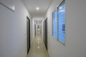 Un pasillo largo y estrecho con puertas a ambos lados y un ventanal grande a la derecha.