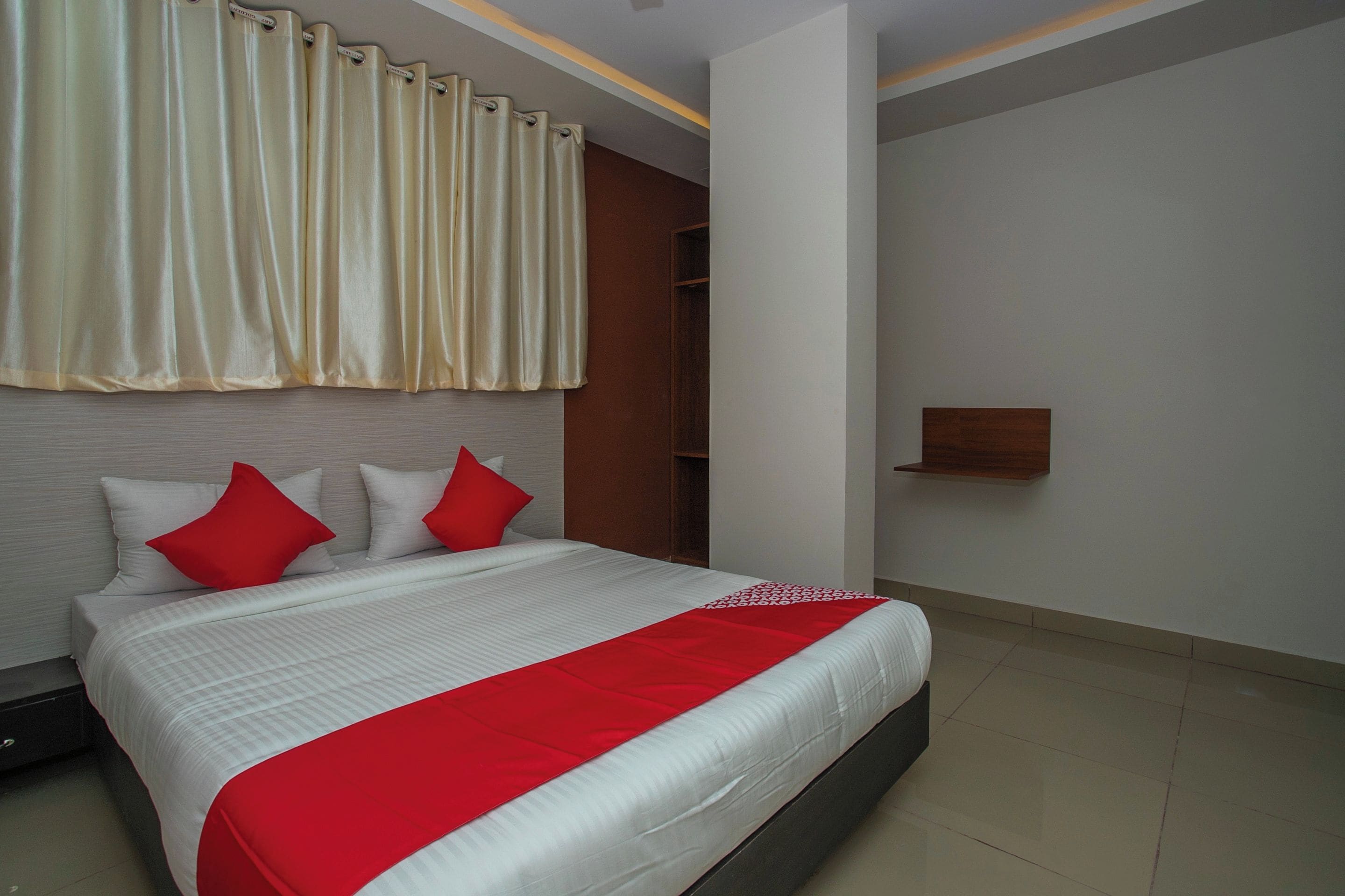 A modern bedroom with a large bed, red and white bedding, a wooden wardrobe, and a wall-mounted shelf.