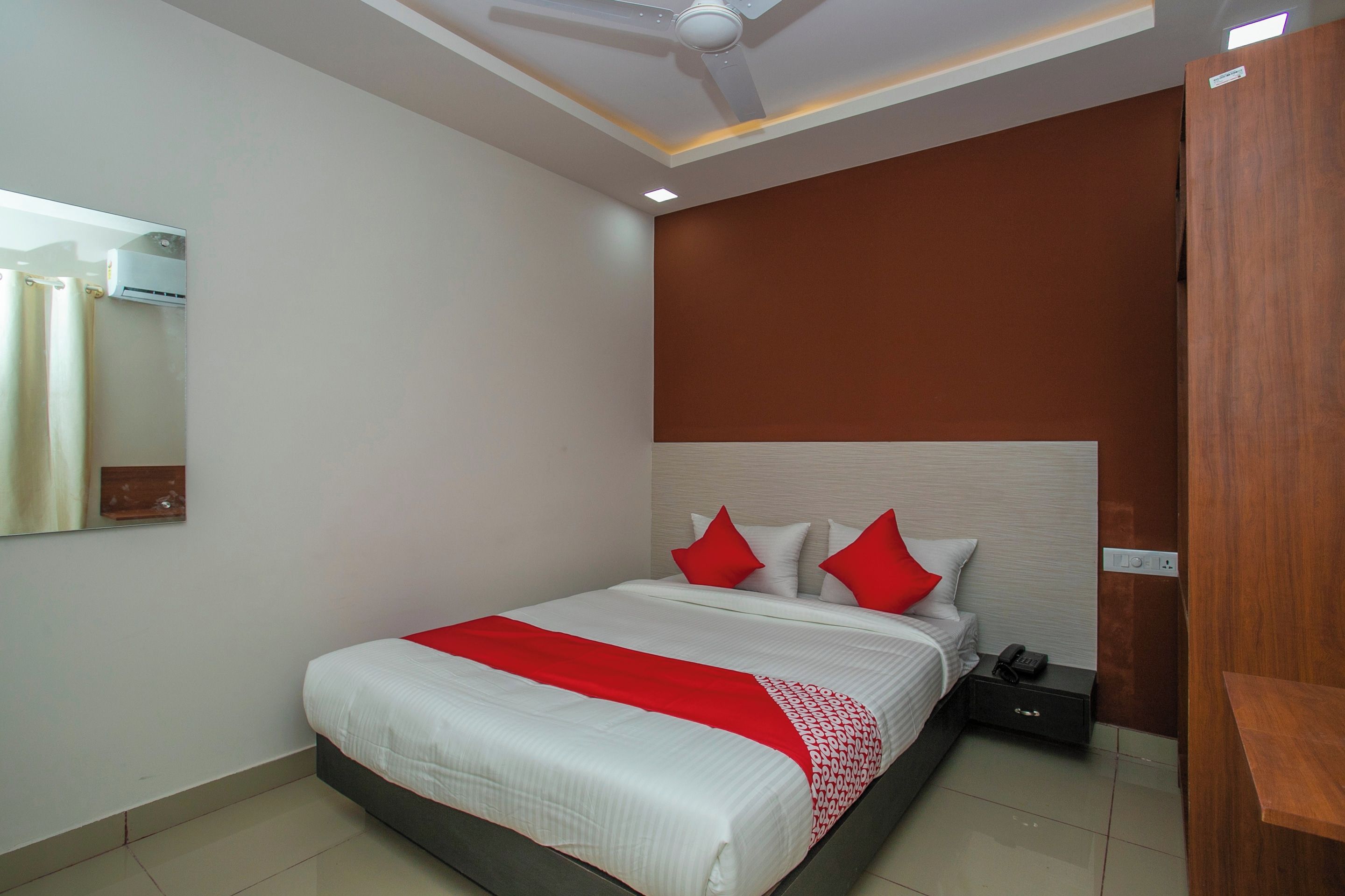 Een hotelkamer met een bed, nachtkastje, telefoon en een spiegel aan de muur.