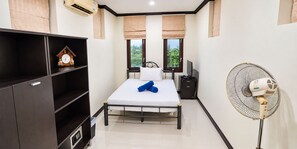 A small, modern room with a bed, a desk with a computer, a wall-mounted air conditioner, and a standing fan. - Private 5-bedroom Pool Villa in Middle of the Island Phuket (Kathu)