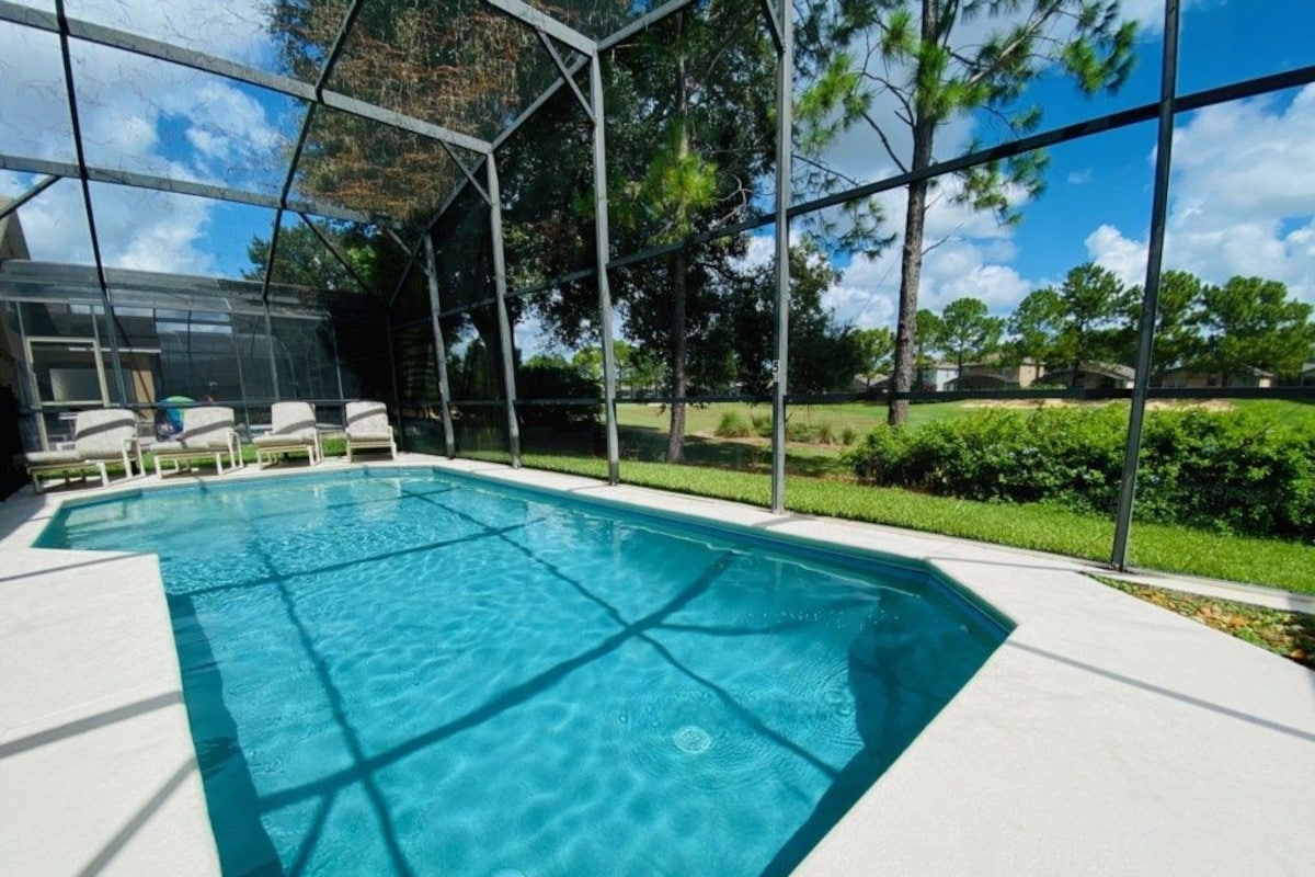 A swimming pool with a glass enclosure, surrounded by a white deck and chairs.