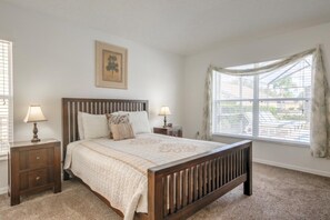 A bedroom with a wooden bed, two bedside tables, a window with curtains, and a wall-mounted picture. - South Facing Pool & Game Room! 6 Bedroom Home (Haines City)