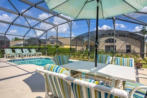 A covered outdoor area with a pool, lounge chairs, and a table with striped cushions. - South Facing Pool & Game Room! 6 Bedroom Home (Haines City)