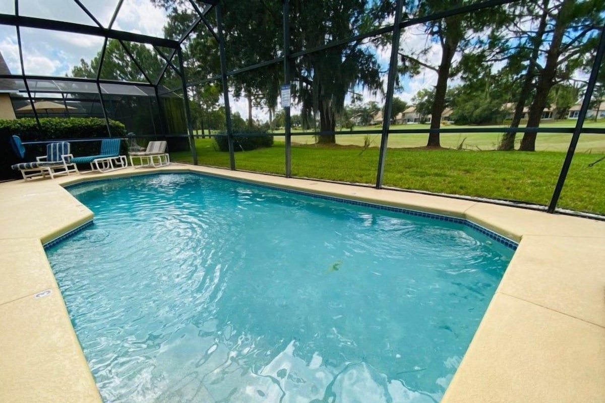 A rectangular swimming pool with a clear blue water surface, surrounded by a beige deck and a glass enclosure.