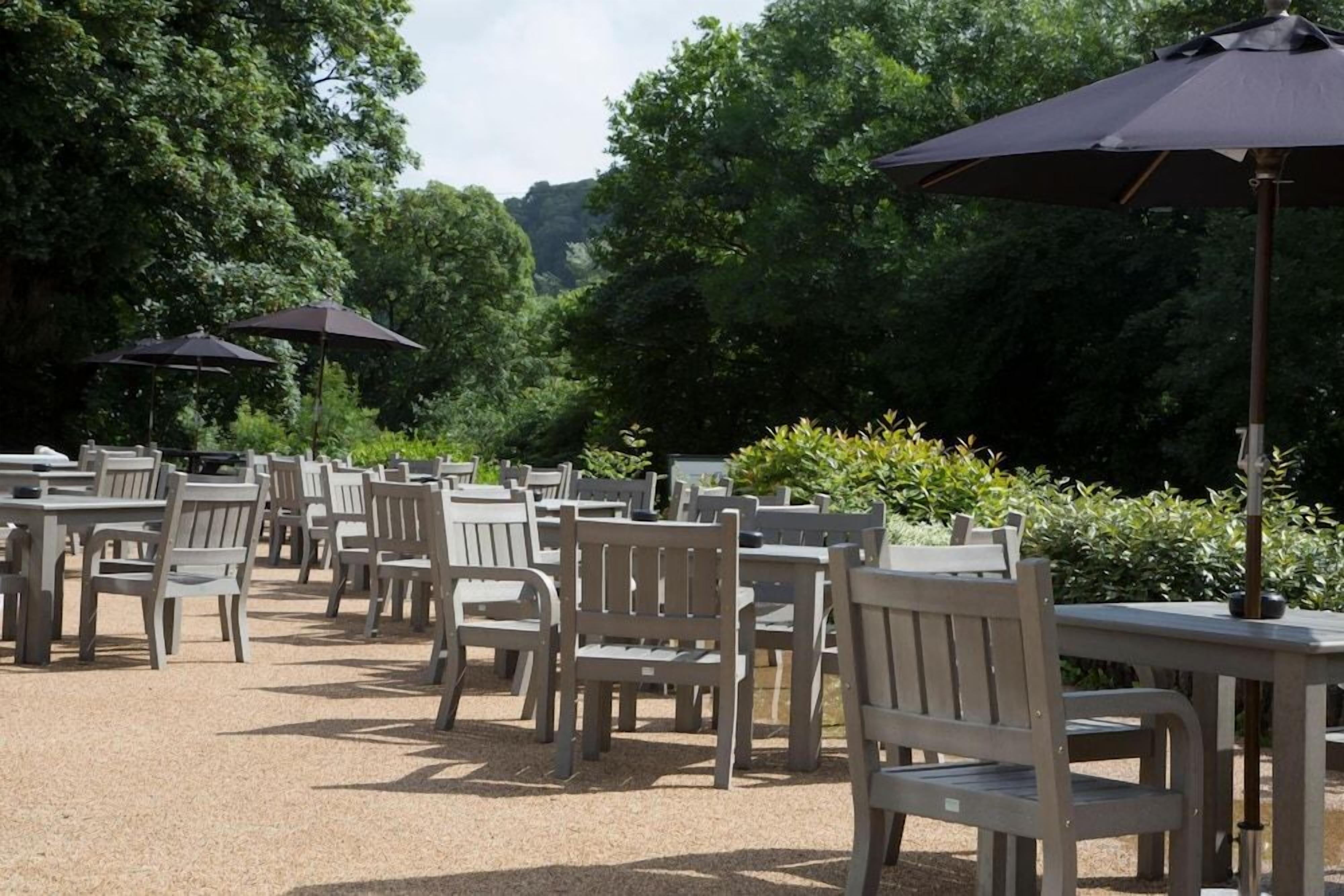 An outdoor seating area with tables and chairs, surrounded by greenery and trees.