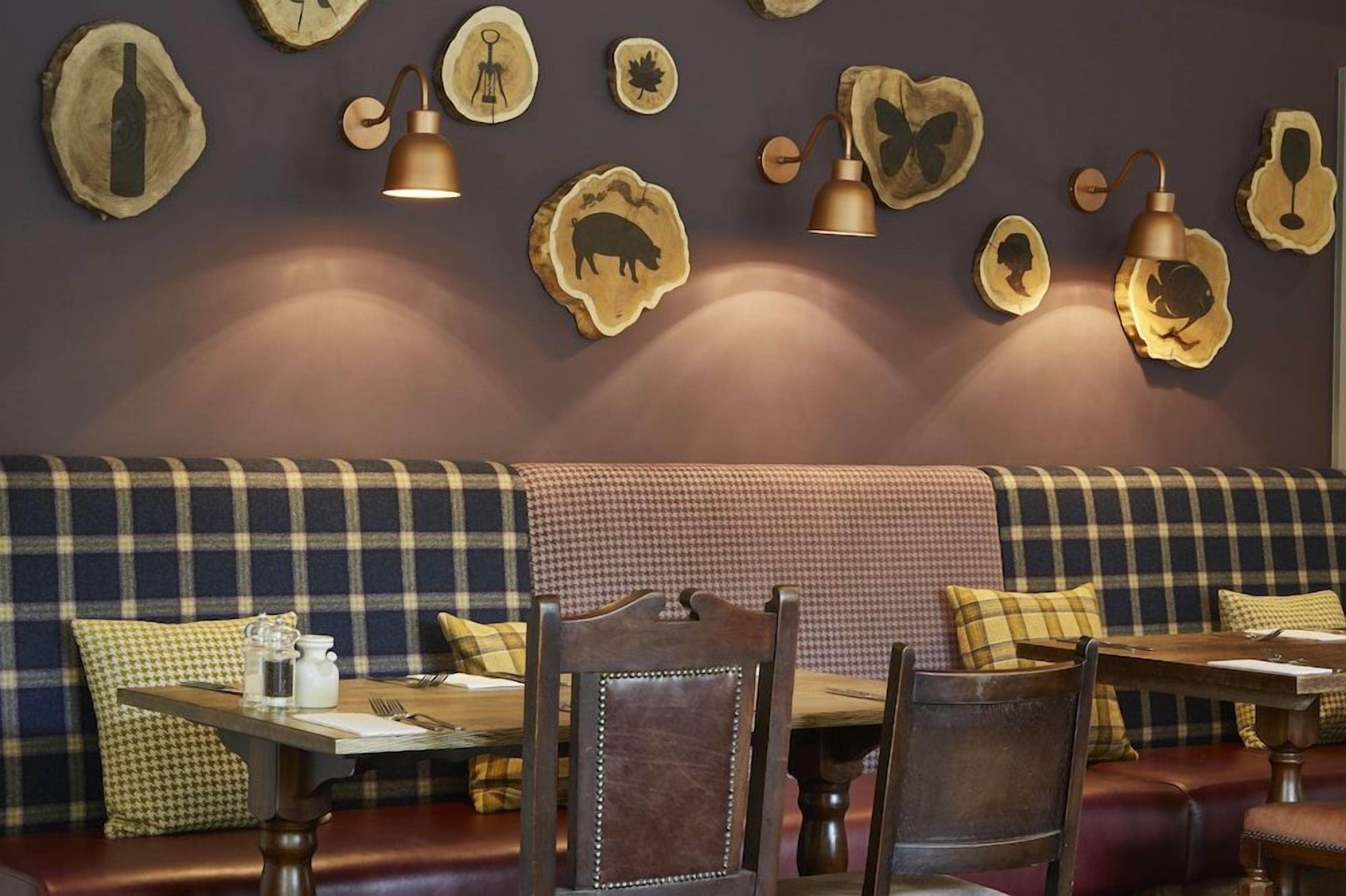 A restaurant interior with a checkered bench seating area, wooden tables, and wall-mounted lighting fixtures.