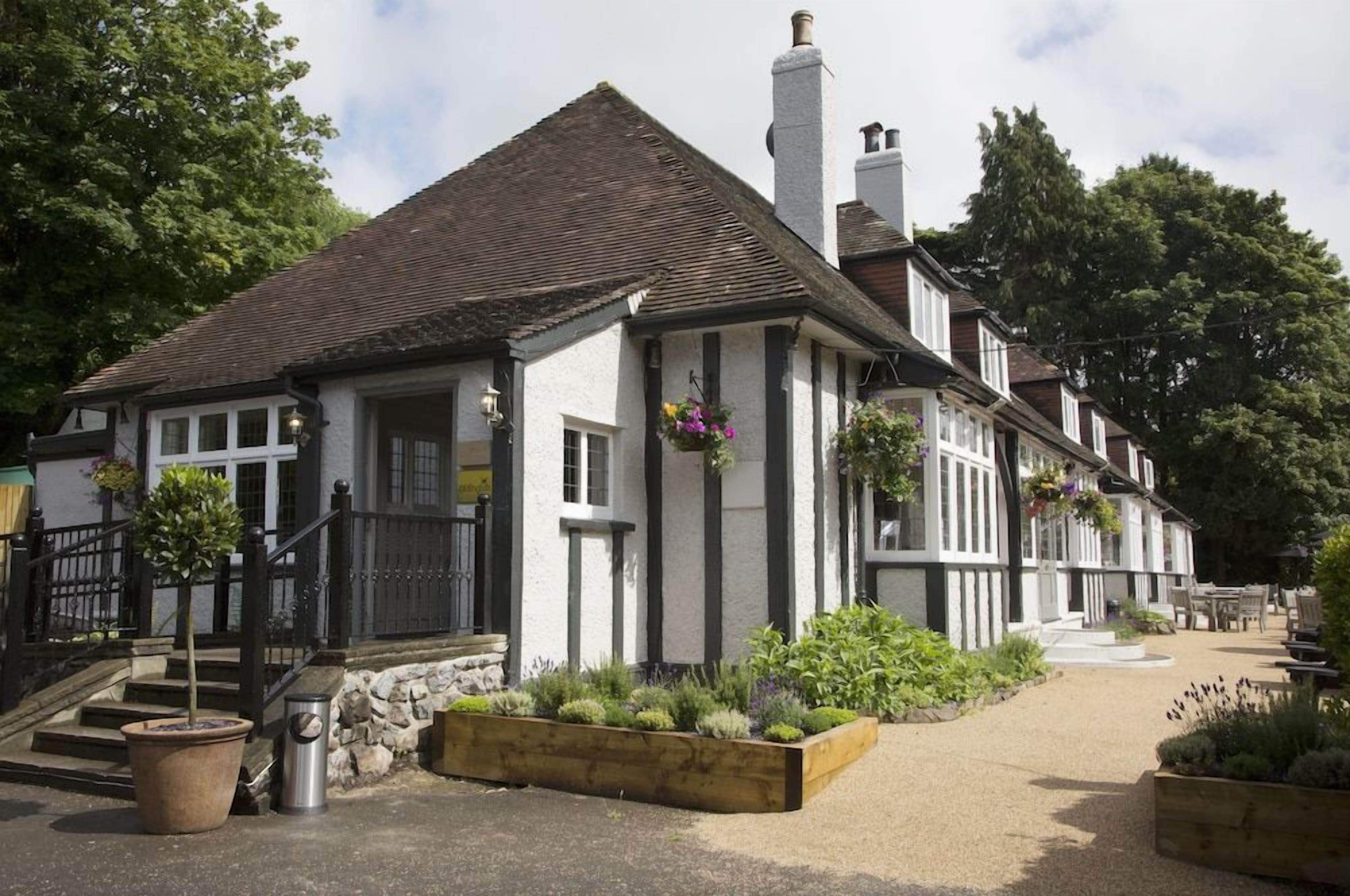 A traditional building with a stone facade, a pitched roof, and a front garden with planters.