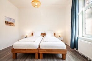Ein Doppelbett mit Holz-Kopfteil, zwei Nachttische mit Lampen, ein Bild an der Wand und ein Fenster mit Vorhängen.