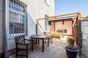Eine Terrasse mit Tisch und Stühlen, eine Holzpergola und Kübelpflanzen.