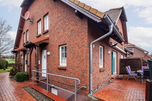Ein rotes Backsteinhaus mit Veranda, Satellitenschüssel und einem kleinen Garten mit Gartenmöbeln.
