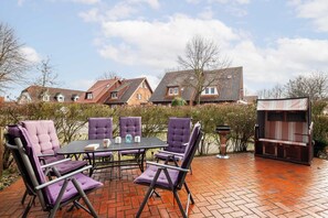 Eine Terrasse mit Tisch und Stühlen, einem Grill und einer Sitzecke mit Blick auf Häuser im Hintergrund.