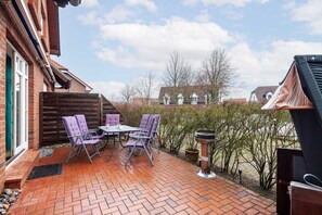 Eine Terrasse mit Backsteinpflasterung, einem Holzzaun und einem Tisch mit Stühlen.