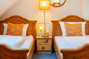 Ein Zimmer mit zwei Holzbetten, einem Nachttisch mit Lampe, einem Buch und einer Kerze.