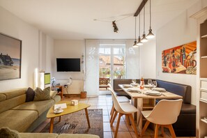 Ein modernes Wohnzimmer mit Sofa, Couchtisch und Essbereich mit Stühlen sowie Tisch, gedeckt für eine Mahlzeit.