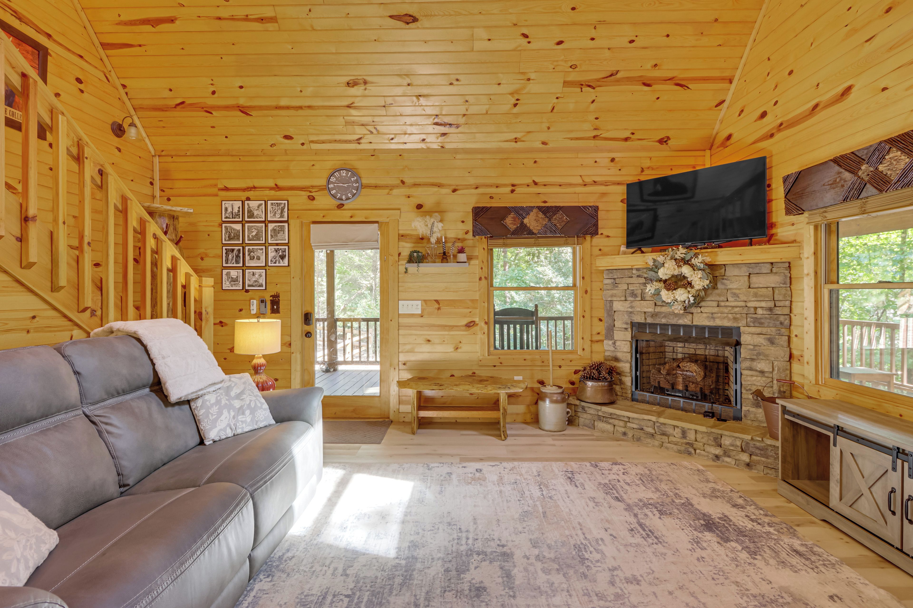 A cozy cabin interior with a leather sofa, a fireplace, a television, and wooden walls.
