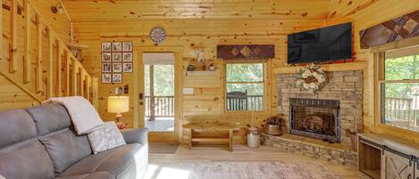 A cozy cabin interior with a leather sofa, a fireplace, a television, and wooden walls.