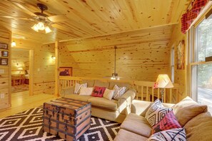 Ein gemütliches Blockhaus-Interieur mit Holzwänden, einer Sofagarnitur, einem gemusterten Teppich und einem Truhenkasten.