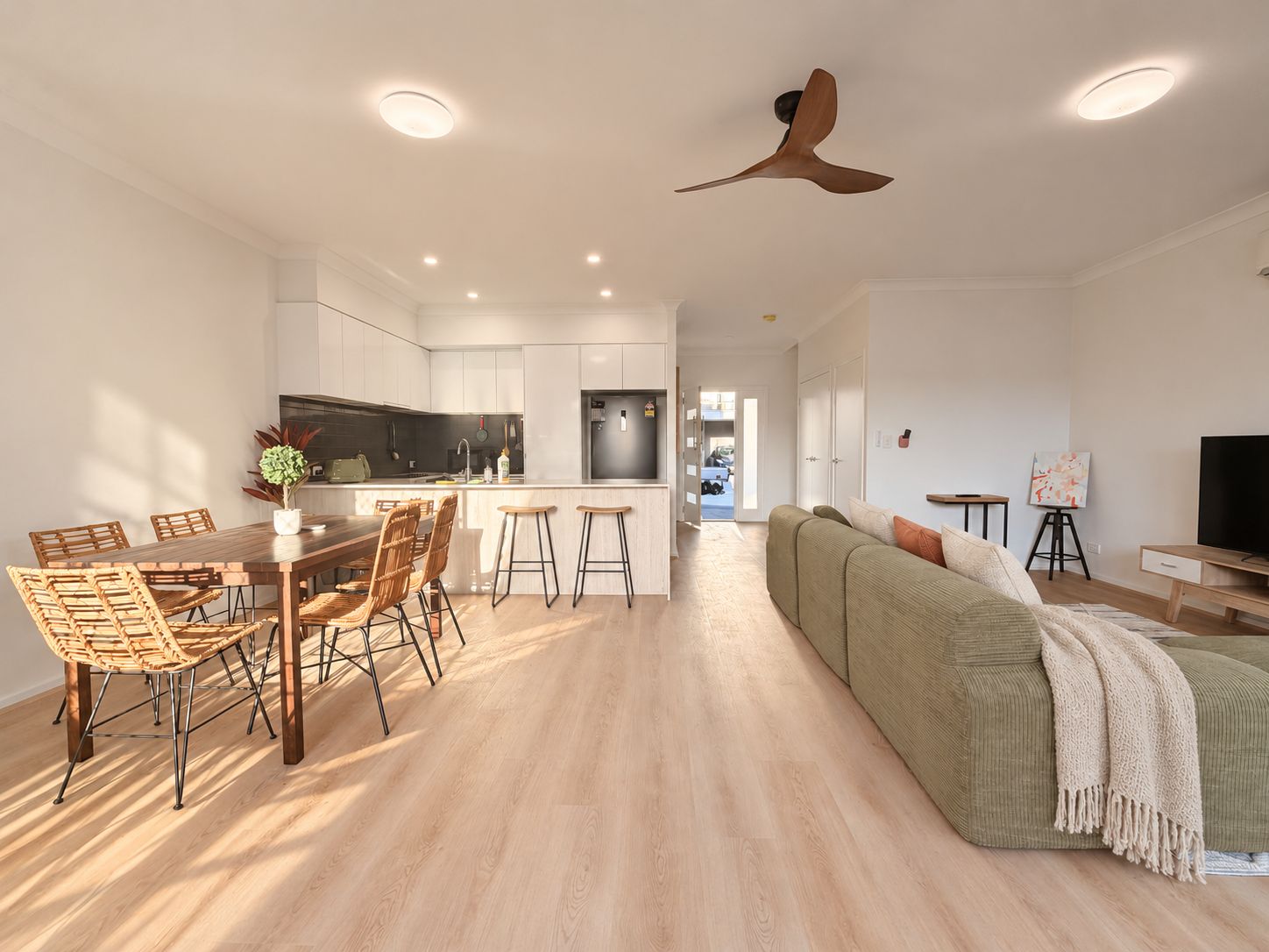 A modern apartment with a dining area, kitchen, living room, and a ceiling fan.