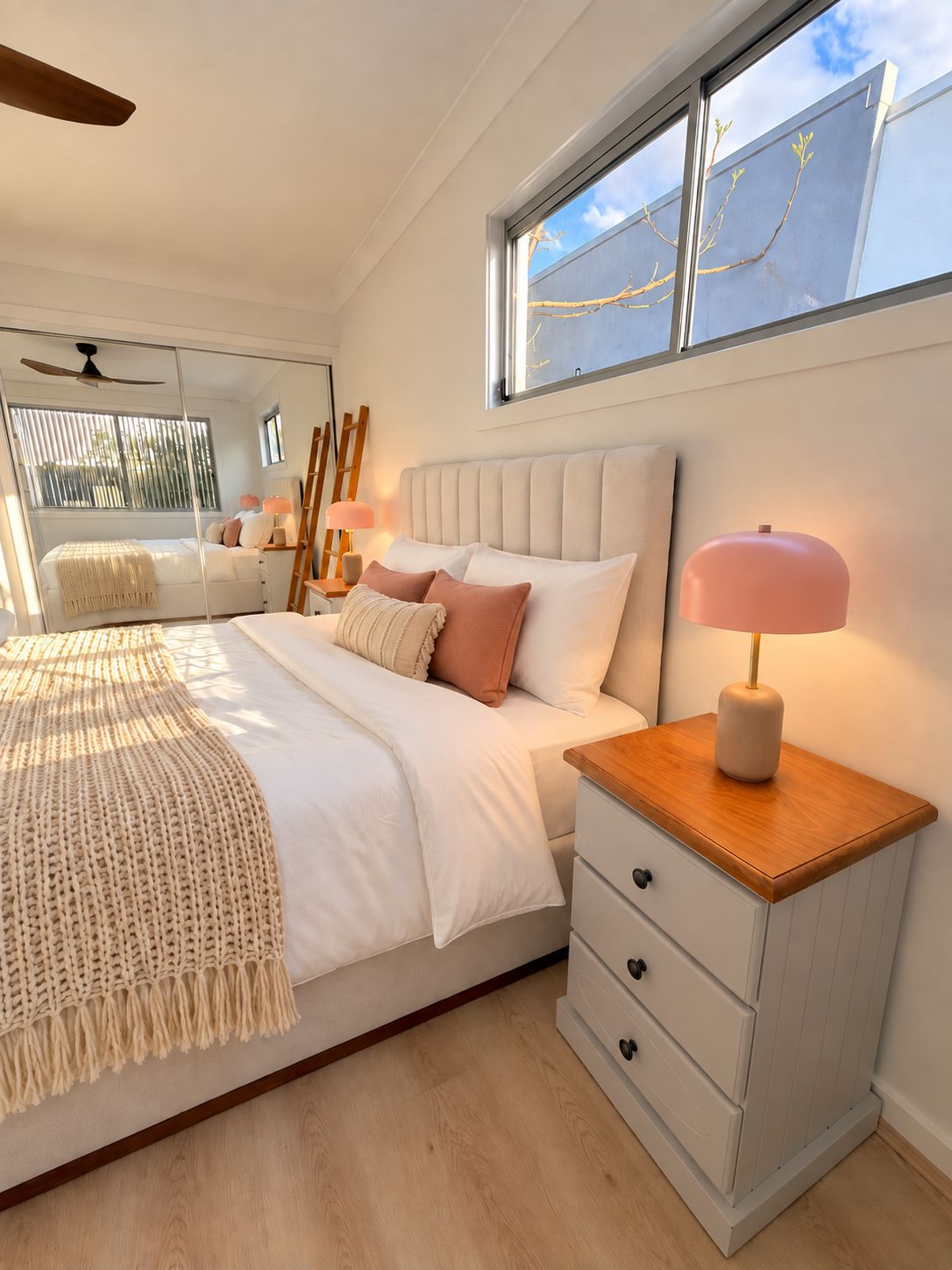 A bedroom with a bed, bedside table, lamp, and a window with a view.