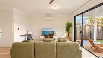 A modern living room with a large window, a flat-screen TV, and a wooden ceiling feature.