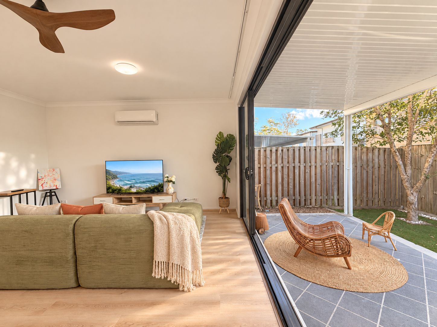 A modern living room with a sofa, television, and a view of the backyard.