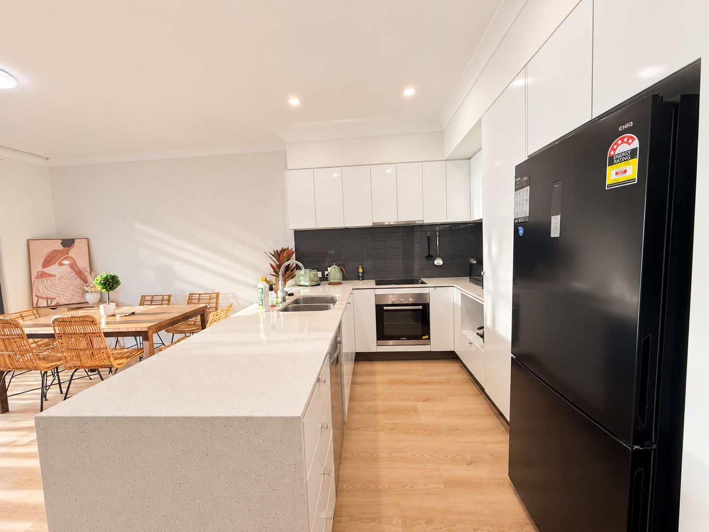A modern kitchen with white cabinets, a black refrigerator, and a wooden dining area.