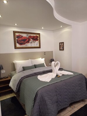 A neatly made bed with a swan towel arrangement, a framed painting of red flowers, and a bedside lamp. - Summit Casarao Da Ducha Hotel (Campos do Jordão)