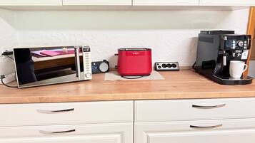 Eine Küchenzeile mit einer Mikrowelle, einem Toaster und einer Kaffeemaschine auf einer Holzausziehtafel, mit Schränken darüber.