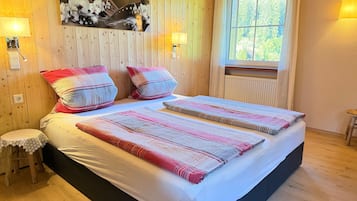 Een tweepersoonsbed met een bedovertrek met patroon, twee kussens, een wanddecoratie, nachtlampjes en een raam met gordijnen.