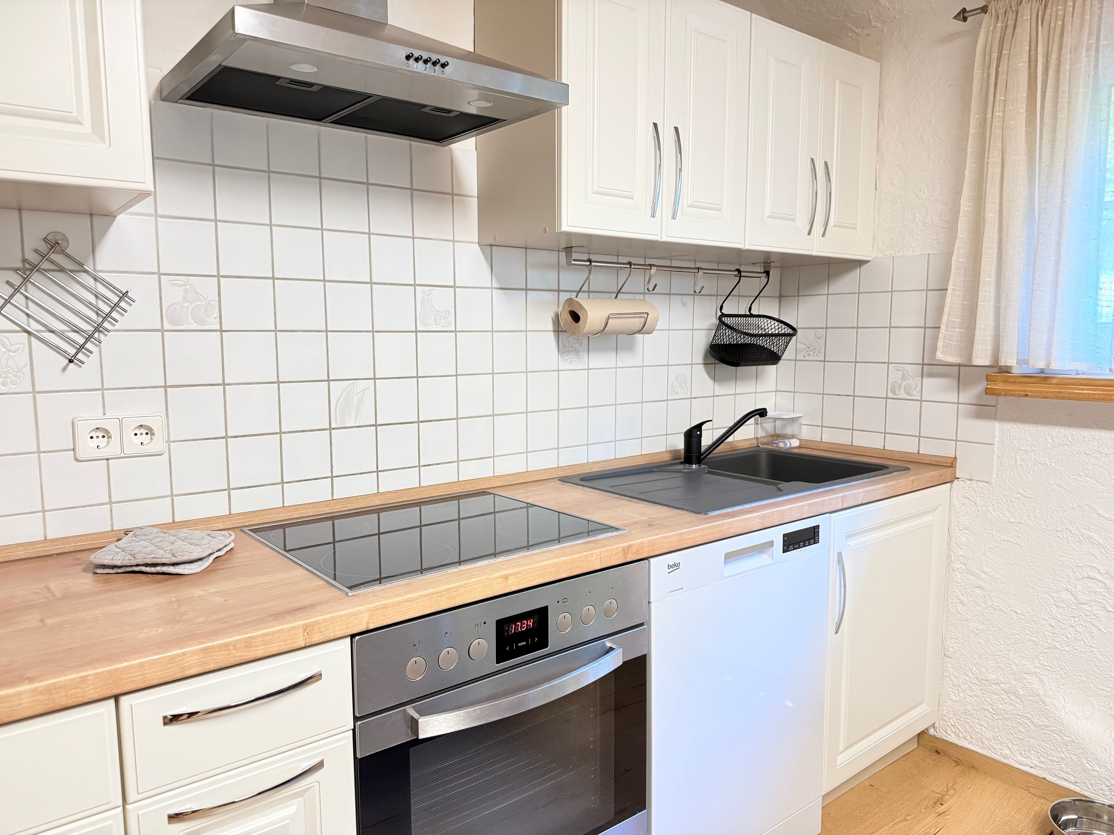 Eine moderne Küche mit weißen Schränken, einer Edelstahl-Dunstabzugshaube, einer Spüle mit zwei Becken und einem Geschirrspüler.