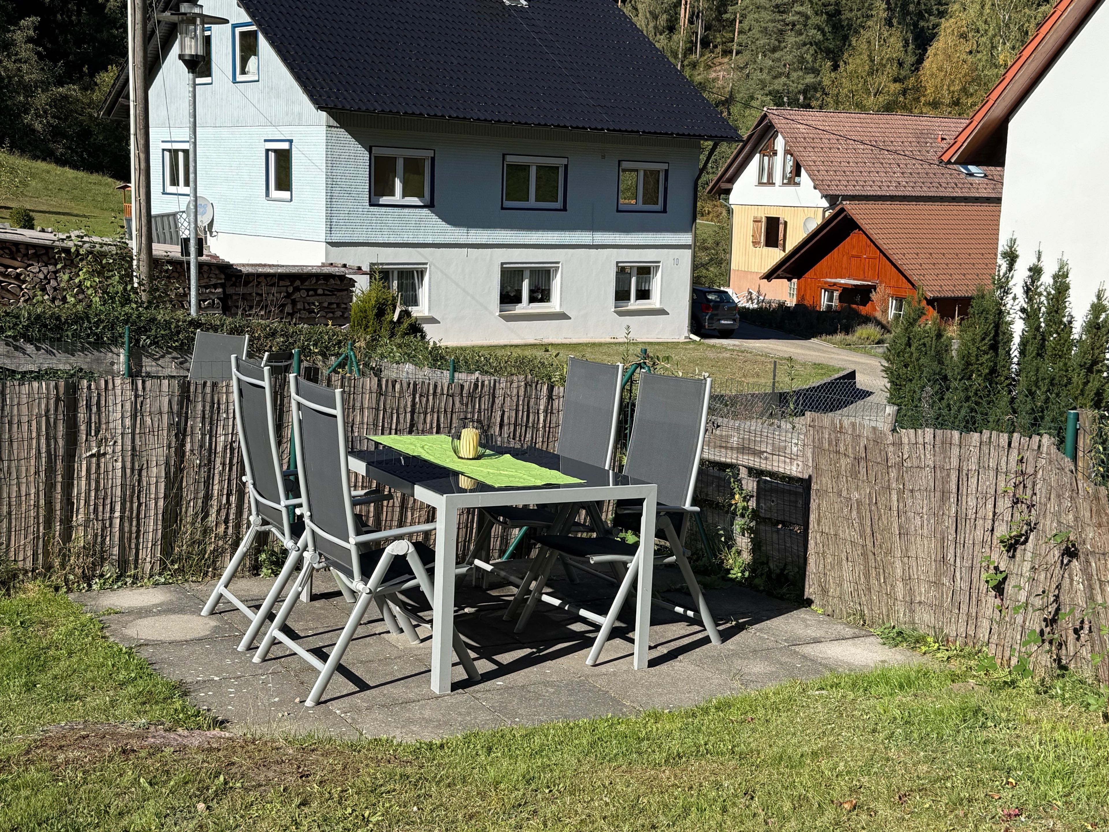 Eine Terrasse mit Tisch und Stühlen, ein Holzzaun und Häuser im Hintergrund.