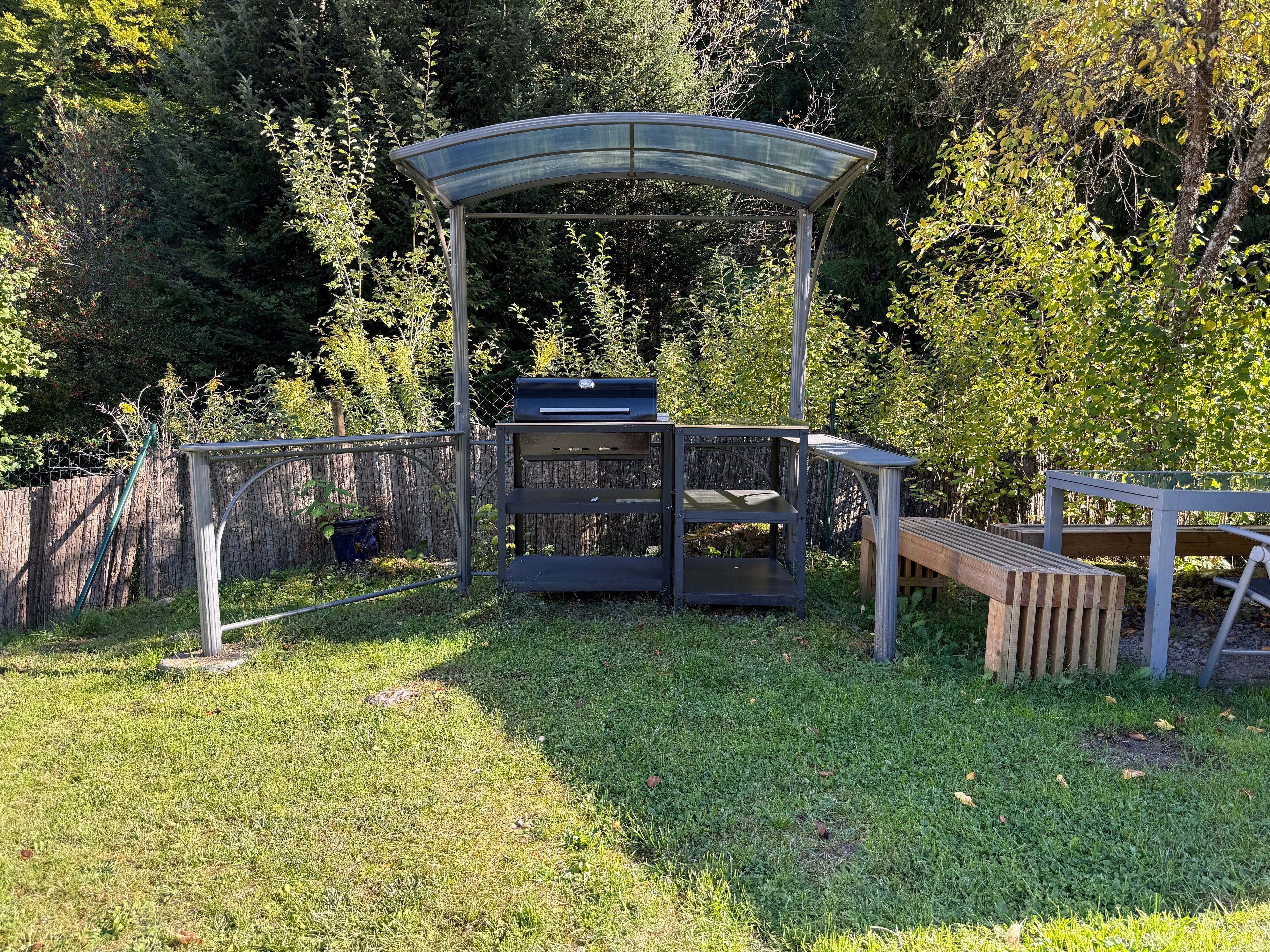An outdoor patio area with a grill, a wooden bench, and a metal pergola.