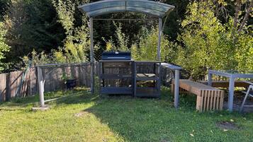 An outdoor patio area with a grill, a wooden bench, and a metal pergola.
