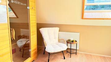 Een kamer met een houten garderobe, een witte fauteuil, een klein tafeltje met een plant en een radiator.