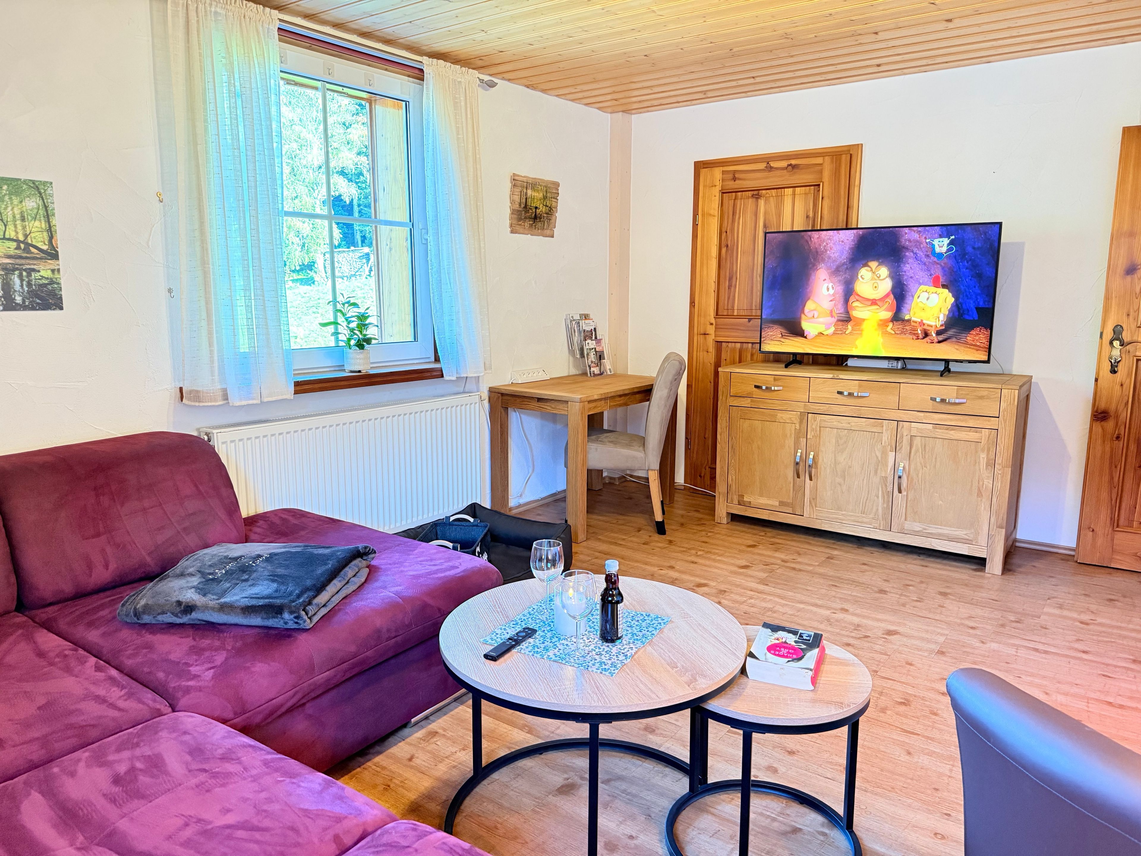Ein Wohnzimmer mit einer Couch, einem Fernseher, einem Holzschrank und einem kleinen Tisch.