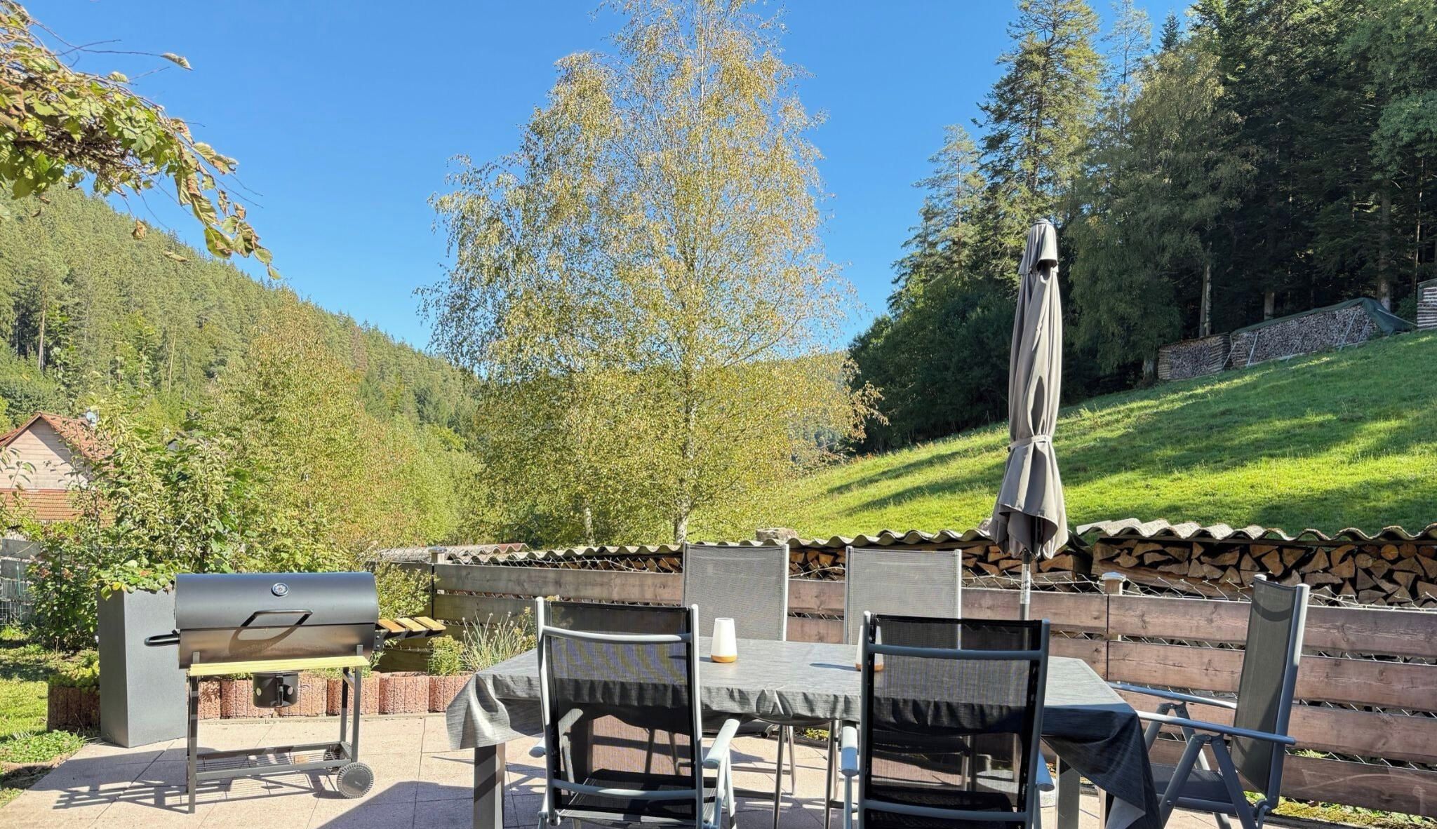 An outdoor dining area with a grill, chairs, and a table.