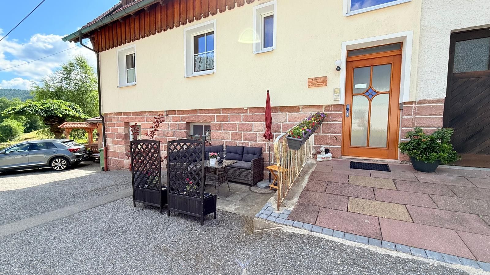 A building with a wooden door, a small outdoor seating area with a table and chairs, and a car parked in front.