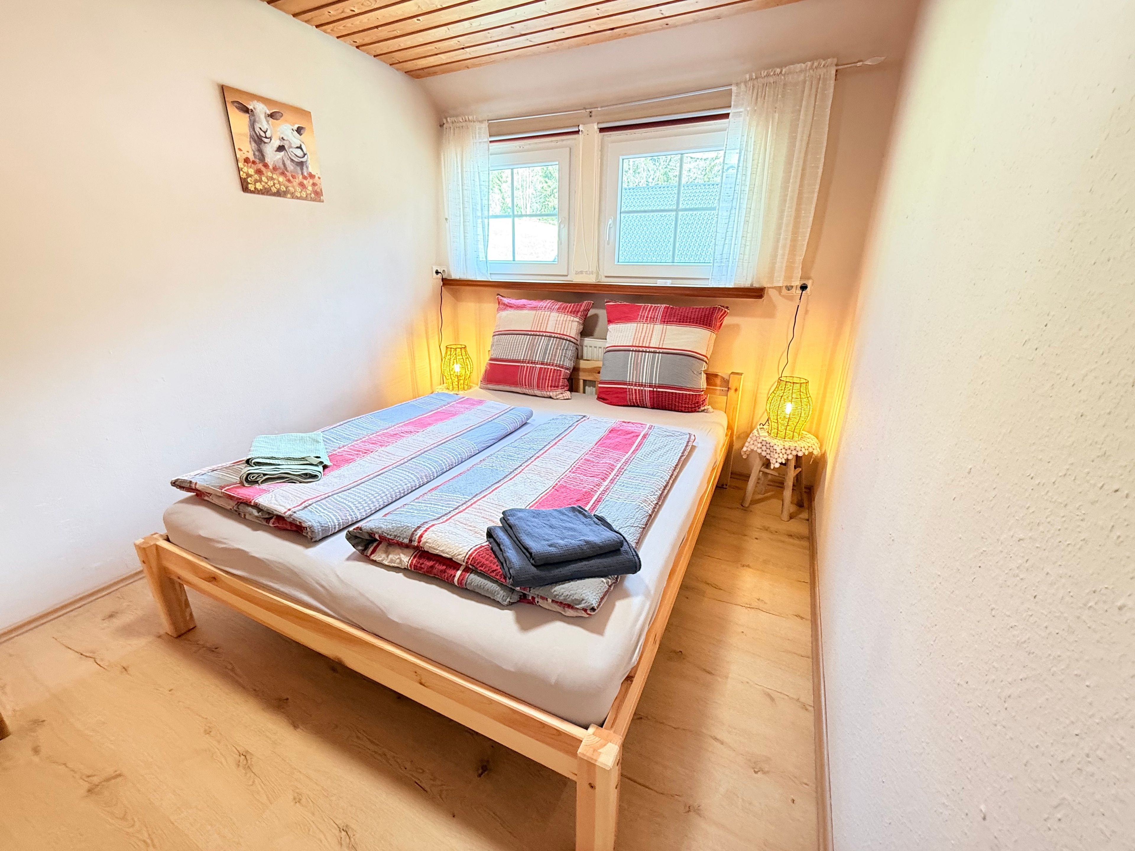 A bedroom with a wooden bed, a window with curtains, a bedside lamp, and a painting on the wall.