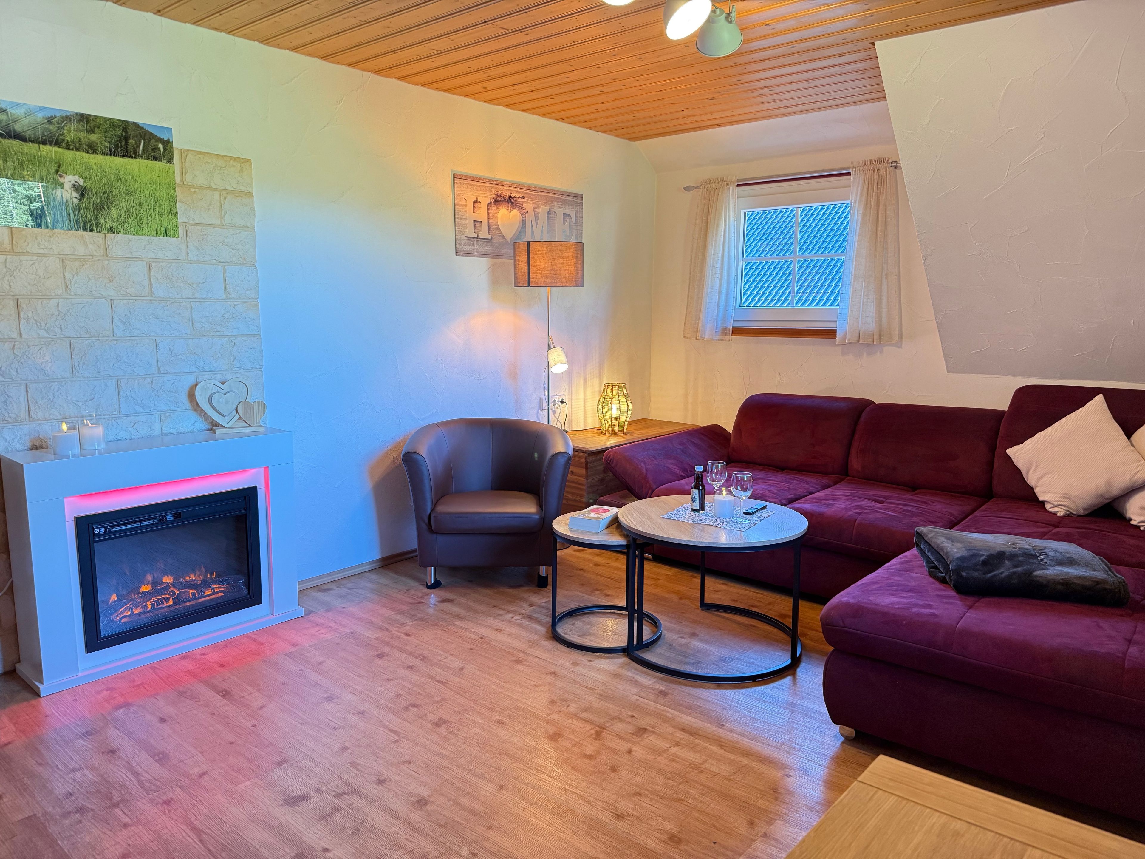 Ein gemütliches Wohnzimmer mit Kamin, einem roten Sofa, einem runden Couchtisch und einem bequemen Sessel.
