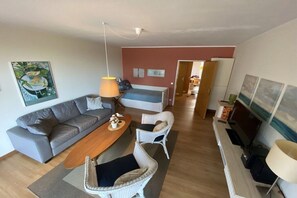 Ein Wohnzimmer mit einer Couch, einem Couchtisch und Korbstühlen. Ein Fernseher und eine Lampe stehen auf einem Beistelltisch.