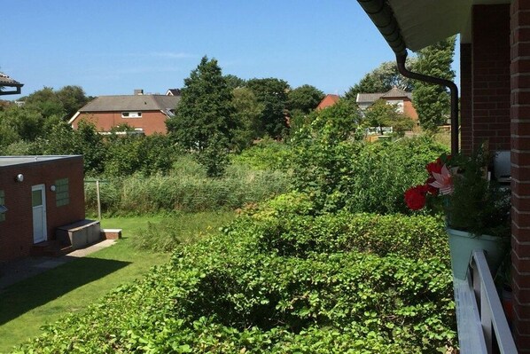 A residential area with a brick house, a garden with green shrubs, and a red flower bed. - Holiday apartment with 3 bedrooms (Borkum)