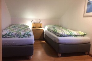 Een kleine, gezellige kamer met twee enkele bedden, een nachtkastje met een lamp en een lijst met een afbeelding aan de muur.