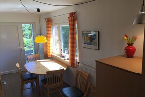 A dining area with a round table, wooden chairs, a red vase with flowers, and a painting on the wall. - Holiday apartment with 3 bedrooms (Borkum)