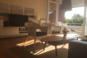 Een woonkamer met rieten meubilair, een flatscreen televisie en een balkon met uitzicht.