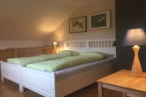 Ein Schlafzimmer mit einem weißen Bett, zwei Kissen, einem Nachttisch mit Lampe und zwei gerahmten Bildern an der Wand.