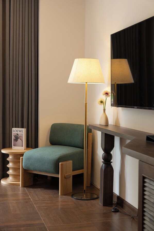 A room with a green sofa, a floor lamp, a small table with a magazine, and a television mounted on the wall. - LARACINE PHU QUOC HOTEL (Phu Quoc)
