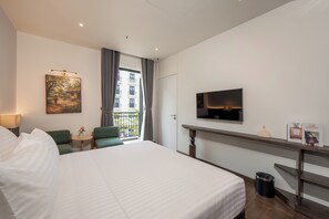 A hotel room with a bed, a desk, a TV, a painting, and a view of the outside. - LARACINE PHU QUOC HOTEL (Phu Quoc)