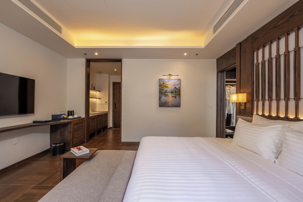 A hotel room with a large bed, a flat-screen TV, a desk with a computer, a painting on the wall, and a walk-in closet.