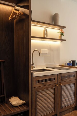 A wooden kitchen with a built-in sink, a hanging clothes rack, and a shelf with a vase and a bottle. - LARACINE PHU QUOC HOTEL (Phu Quoc)